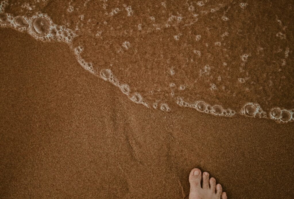 a foot standing on the sand as a calm wave washes over the foot.