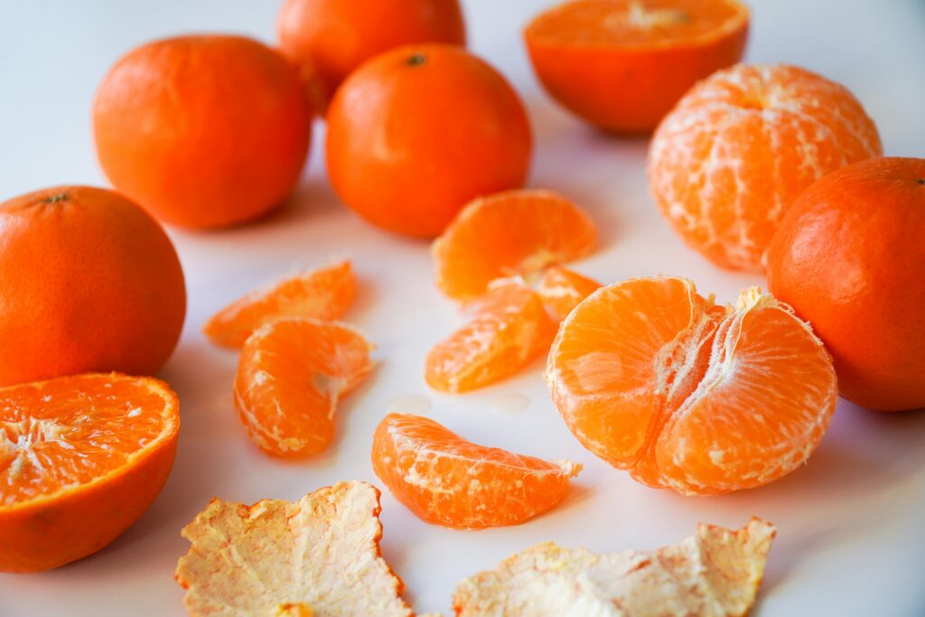 several oranges on a table. Some unopened, some peeled on a white surface.